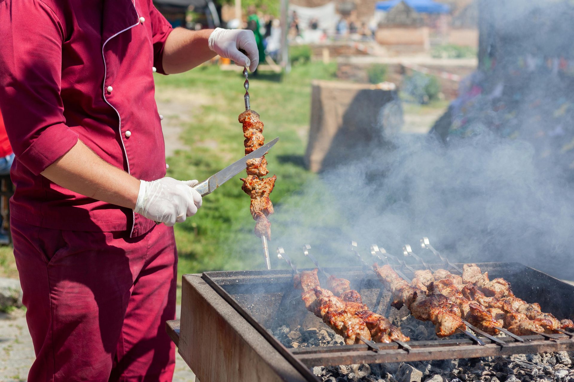 Ein Koch grillt Fleisch im Freien und schneidet Spieße über einem Holzkohlegrill, wodurch ein köstliches Raucharoma entsteht.